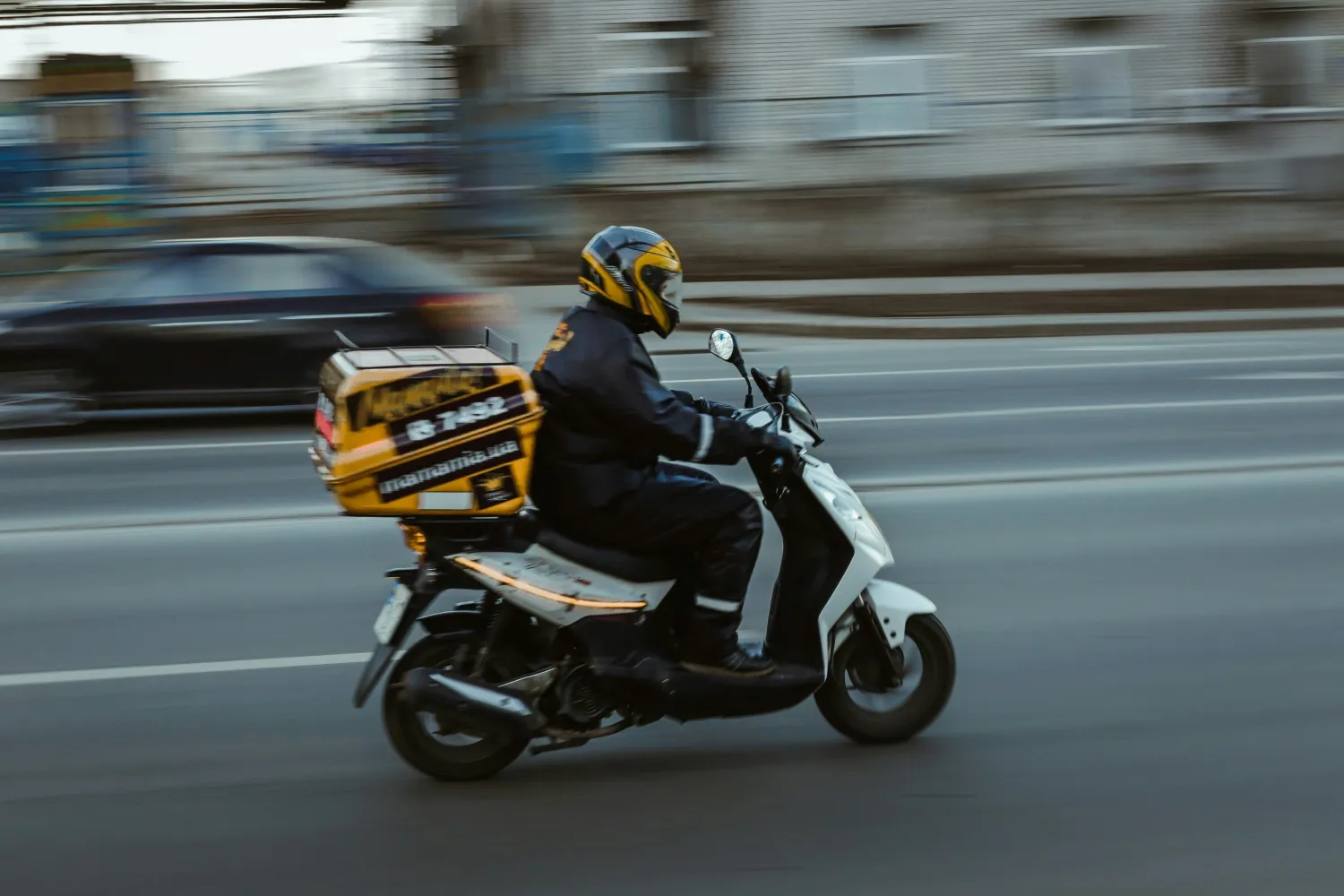 A courier delivery driver driving a moped.