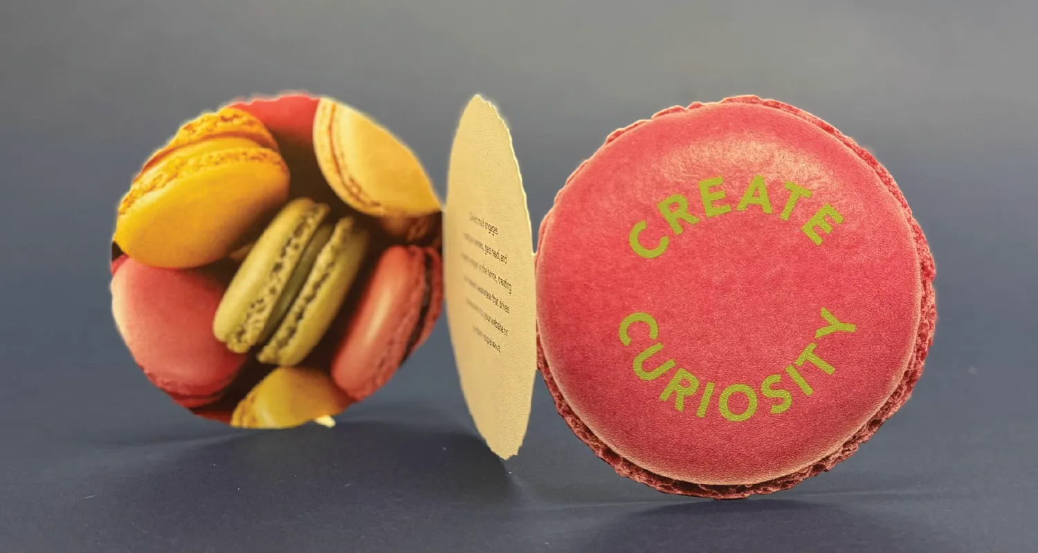 An image of a macaroon shaped trifold business card that reads Create Curiosity