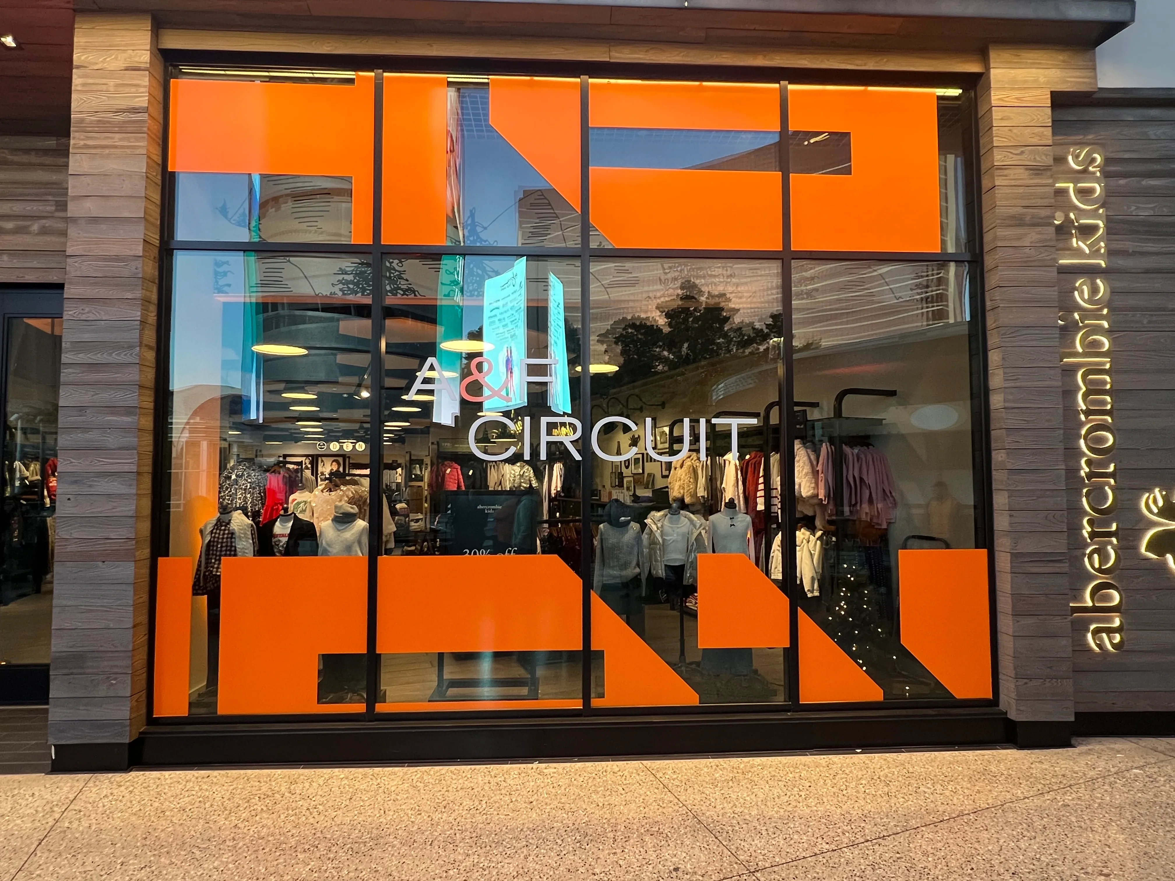 Bright orange vinyl window decals with modern geometric designs for A&F Circuit pop-up at Las Vegas retail storefront, drawing attention from passersby.